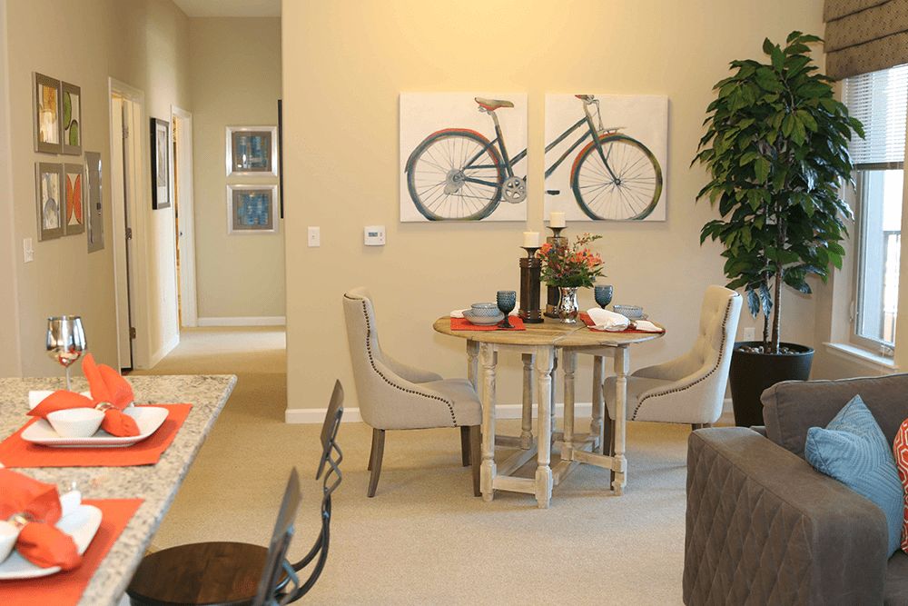 A cozy dining room with a round table, paired chairs, and bicycle-themed artwork on the wall.