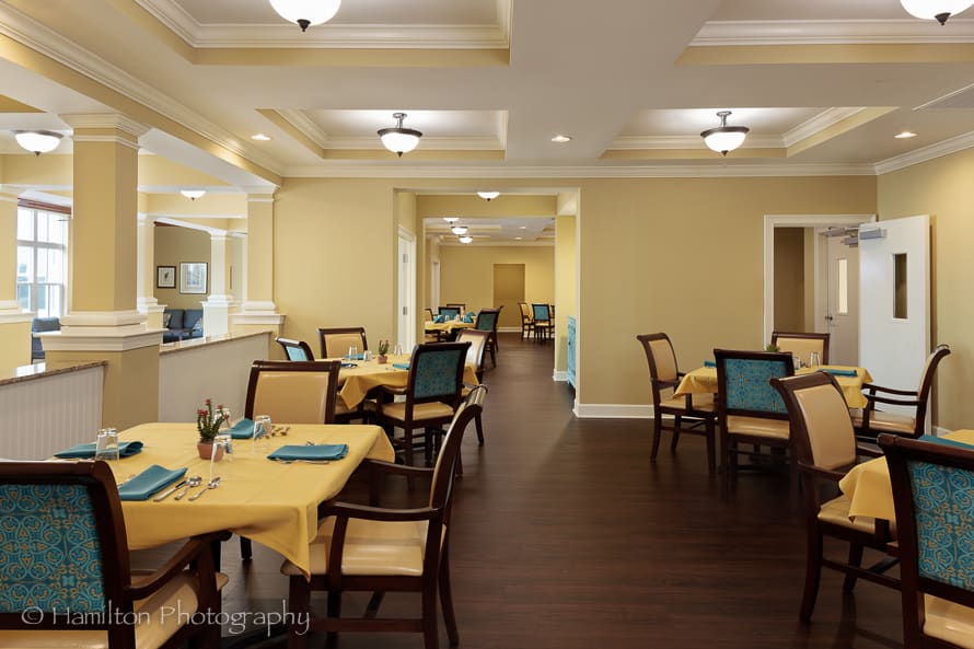 A cozy dining area with neatly arranged tables and chairs, featuring yellow tablecloths and warm lighting.