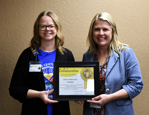 Two women proudly displaying a recognition award during an event.