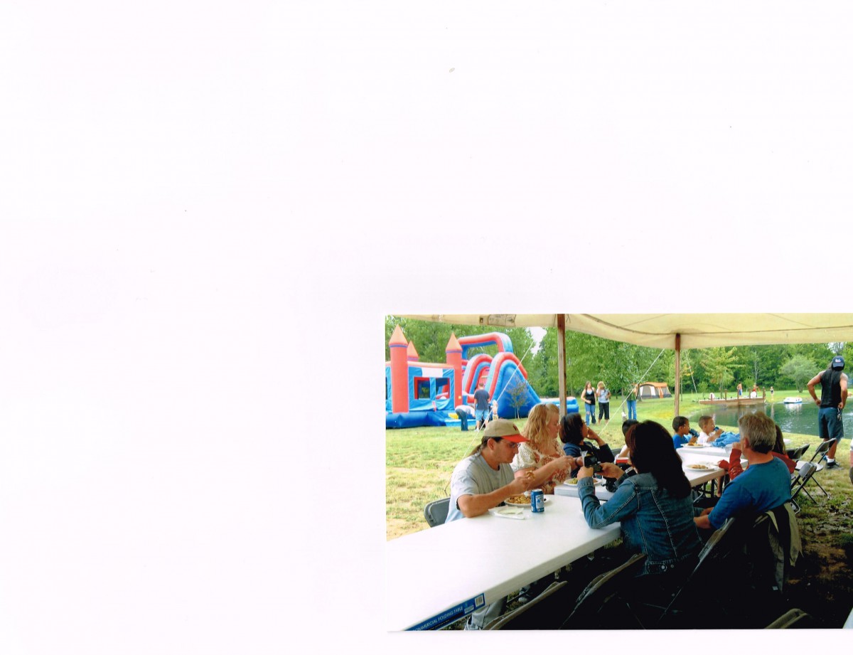 A group of people gathering under a tent at an outdoor event with a bouncy castle in the background.