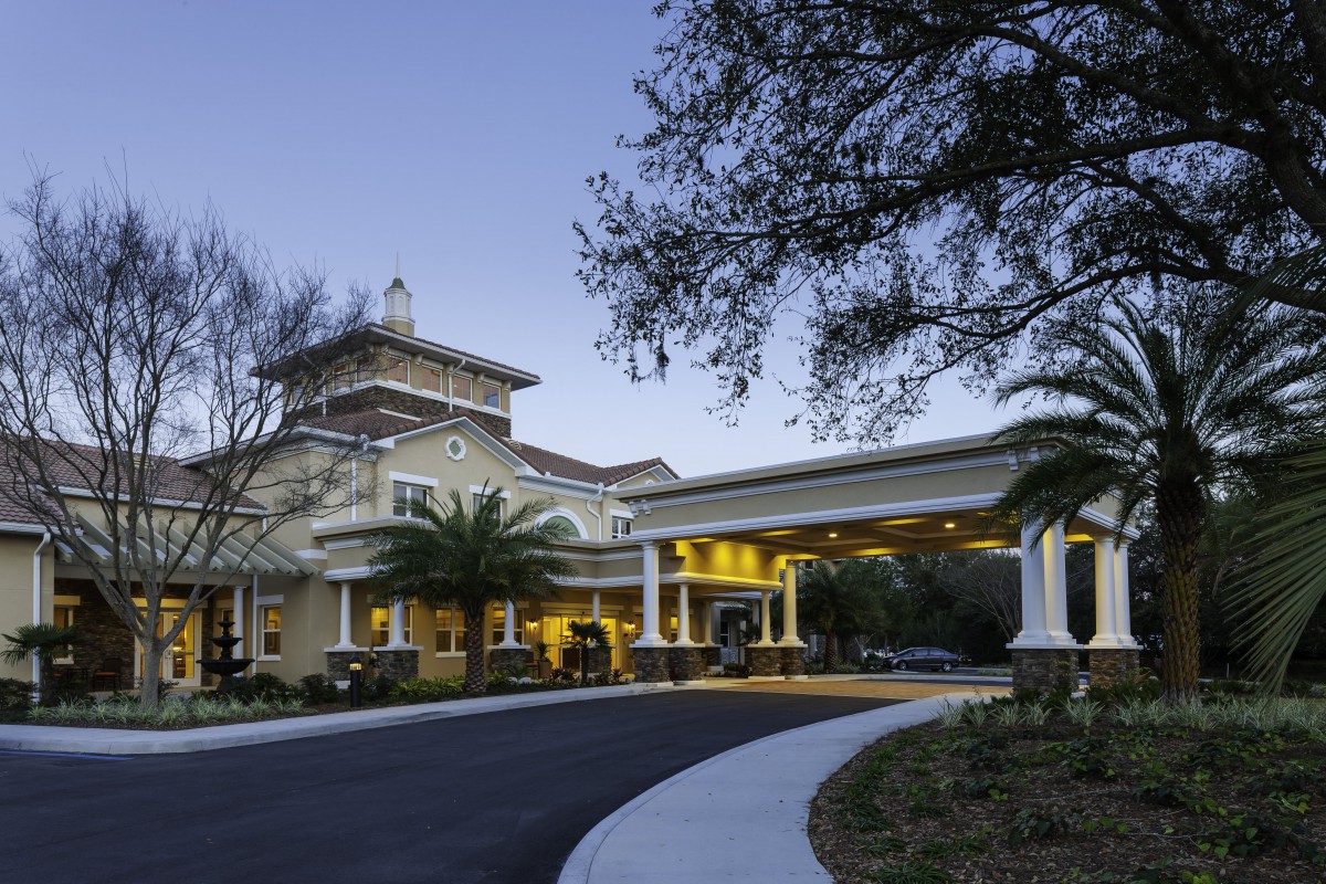 A well-lit building entrance surrounded by palm trees during the evening.