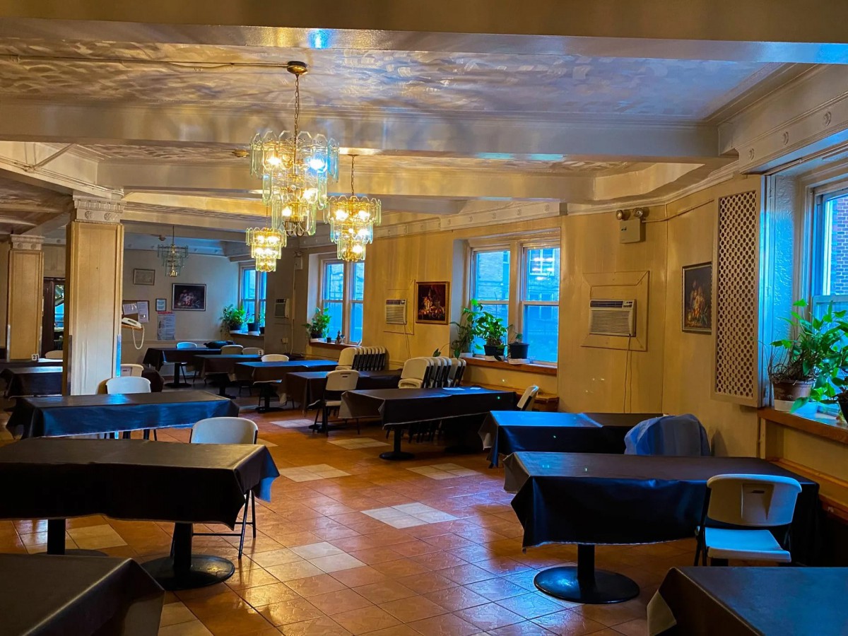 A cozy restaurant interior featuring elegantly set tables, chandeliers, and large windows.
