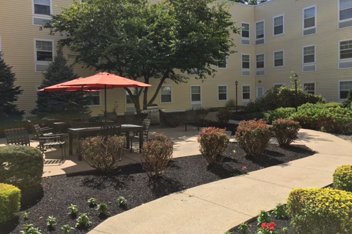 A peaceful patio area with a red umbrella, benches, and lush landscaping outside a residential building.