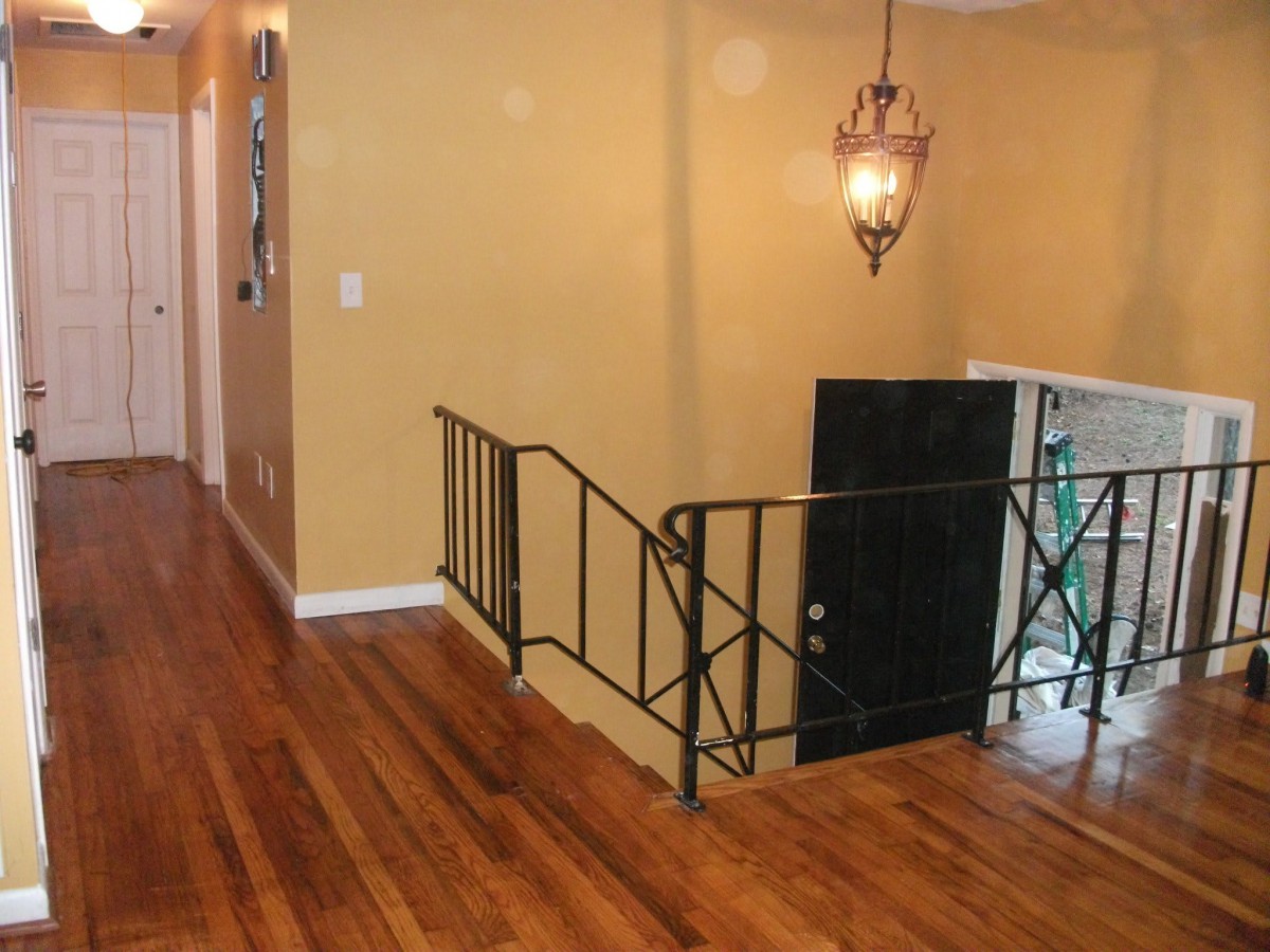 A hallway with wooden flooring, featuring a staircase with metal railings and a decorative lighting fixture.