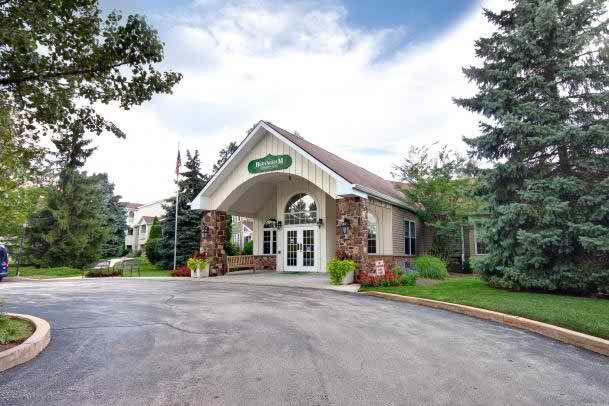 Front view of a building entrance surrounded by trees and landscaping.