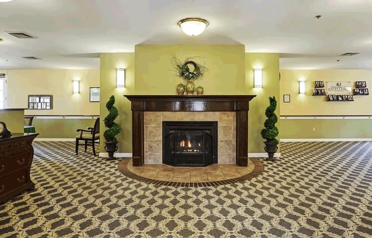A warmly decorated lobby featuring a central fireplace with surrounding plants and patterned carpet.