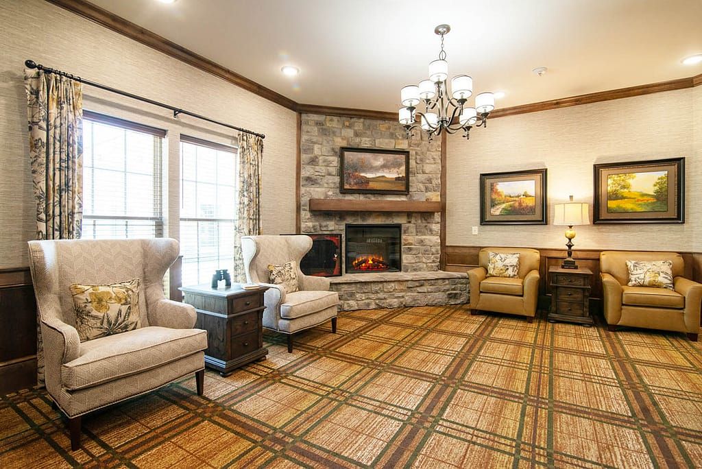 A cozy living room featuring a stone fireplace, comfortable armchairs, and a chandelier.