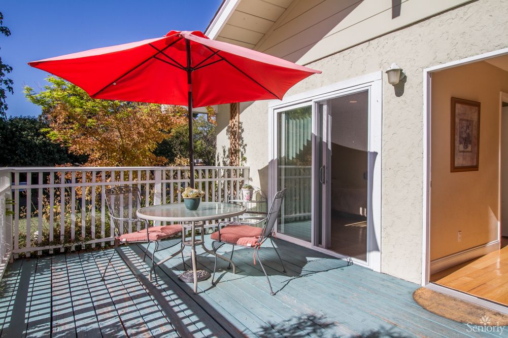 A sunny patio with a red umbrella, table, and chairs.