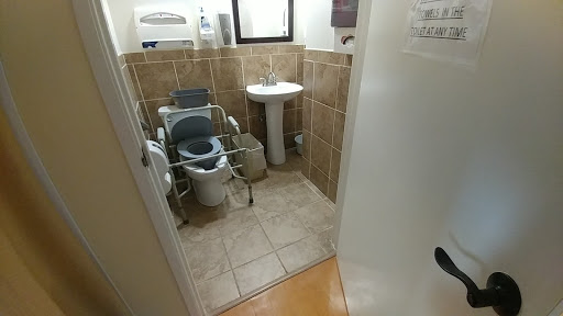 A view of a small accessible bathroom featuring a toilet, sink, and tiled walls.