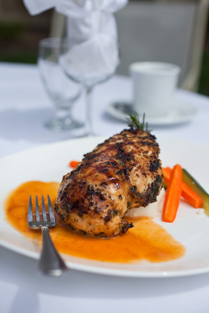 A beautifully plated grilled chicken breast served with a rosemary garnish, accompanied by carrots and zucchini.