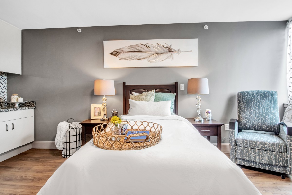 A cozy bedroom featuring a neatly made bed with a decorative tray, flanked by lamps on wooden nightstands and adorned with wall art.