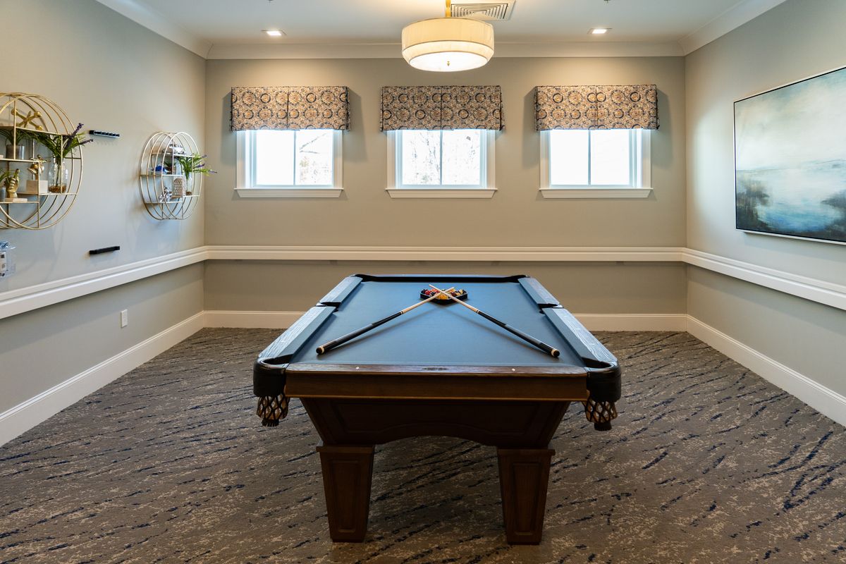 A well-lit game room featuring a pool table with cues neatly arranged.