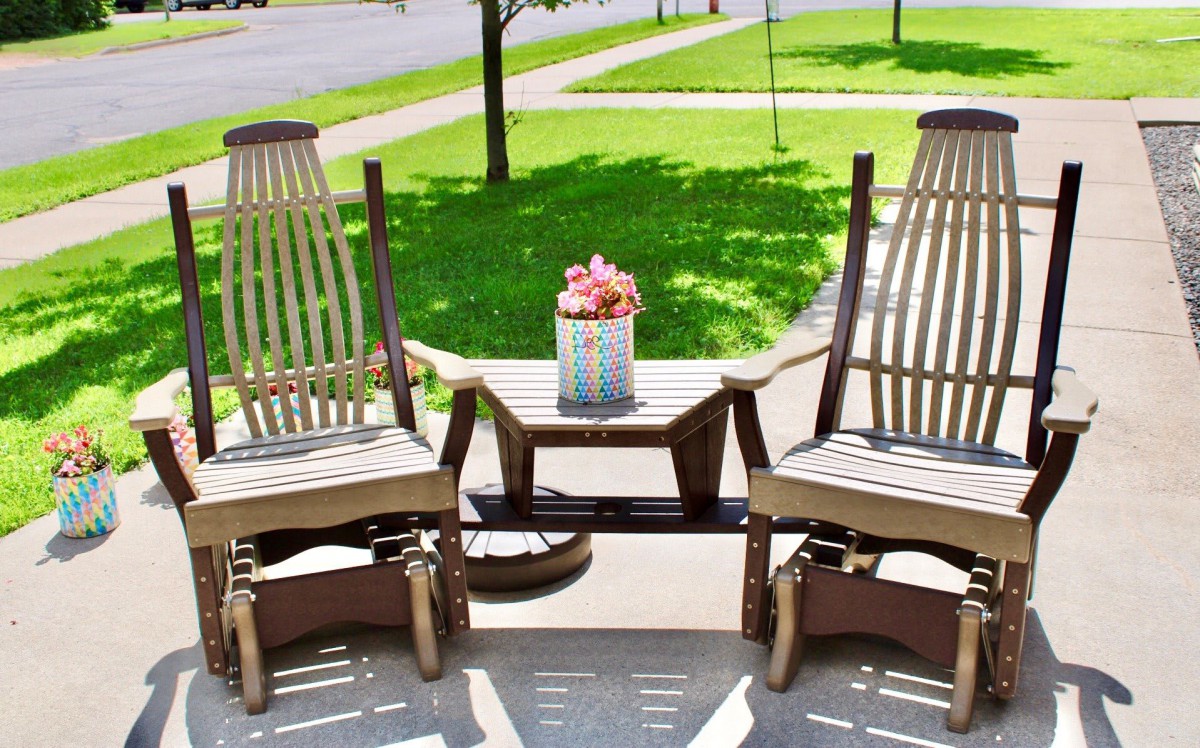 Two rocking chairs and a table with a flower arrangement on a sunny patio.