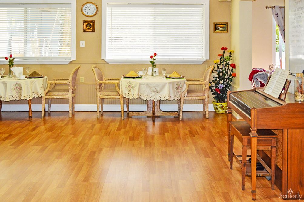 A cozy dining room with a small table set for two, featuring hardwood flooring and decorated with indoor plants and wall art.