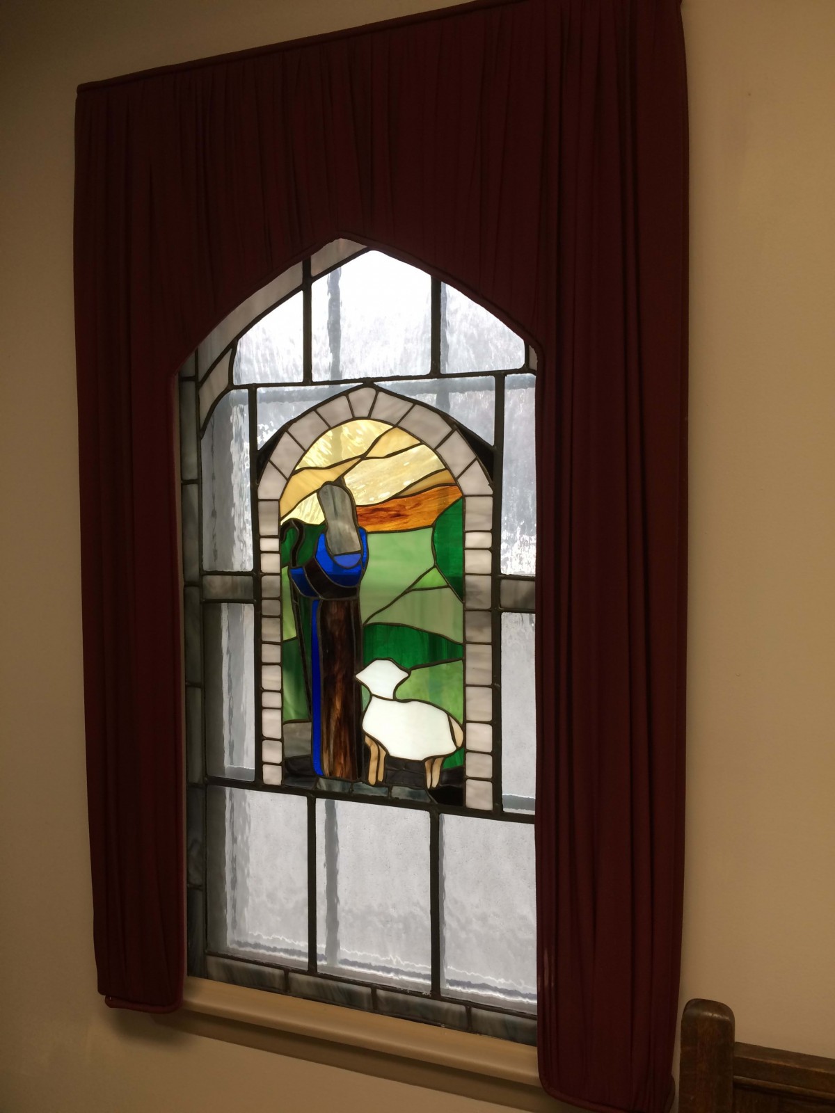 A stained glass window depicting a shepherd with sheep against a scenic background.