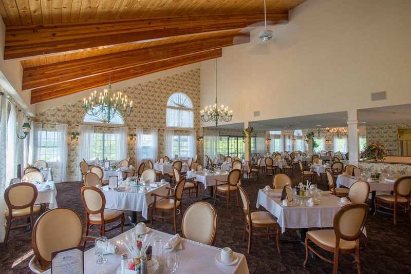 An elegant restaurant dining room with neatly arranged tables and chairs, large windows, and decorative chandeliers.