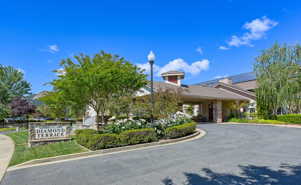 A scenic view of a building surrounded by a landscaped garden and driveway under a clear blue sky.