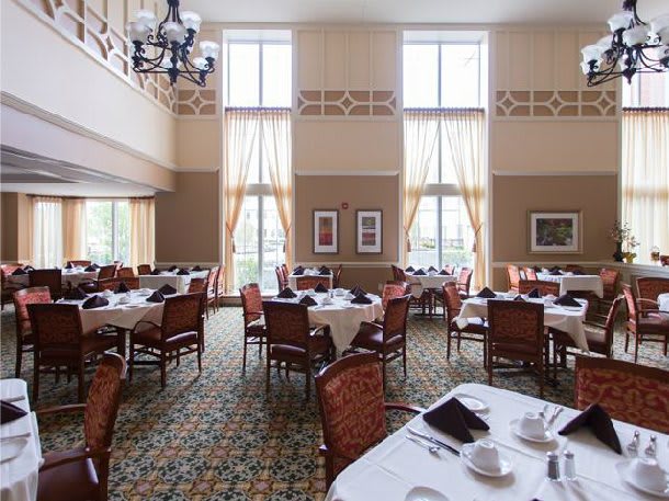 An elegant dining room with neatly arranged tables and chairs, featuring large windows and a chandelier.
