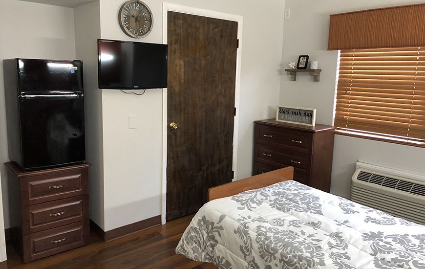 A cozy bedroom with a television mounted on the wall, wooden furniture, and a neatly made bed.