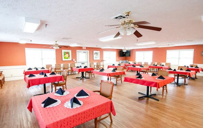 An empty dining room with red tablecloths and neatly arranged tables, featuring ceiling fans and casual decor.
