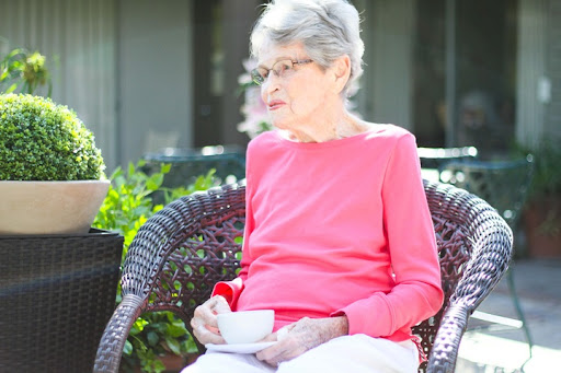 An elderly woman enjoying a quiet moment with a cup of tea in a serene outdoor setting.