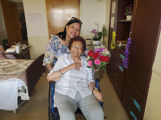 A joyful moment shared between a caregiver and an elderly woman in a wheelchair surrounded by beautiful flowers.