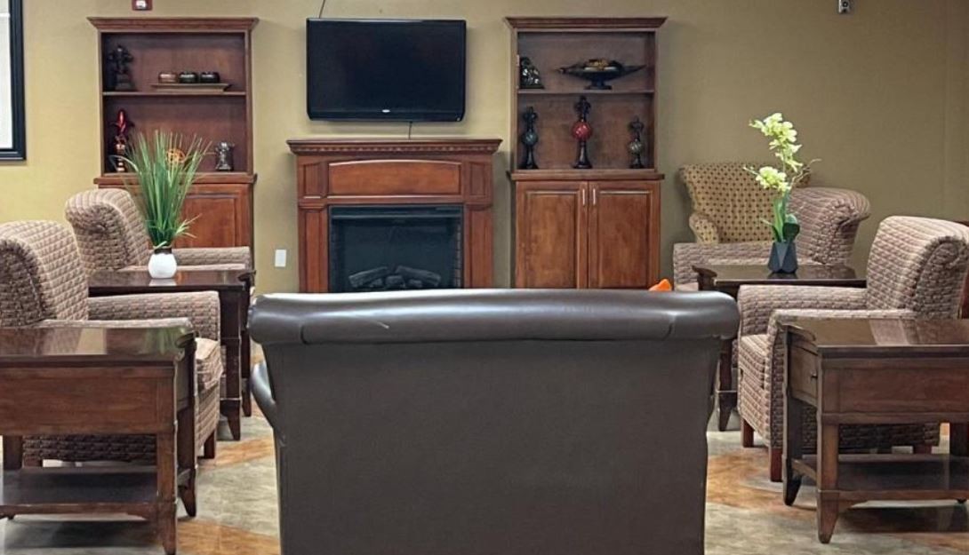 A cozy living room with a TV mounted above a fireplace, surrounded by shelves and seating.