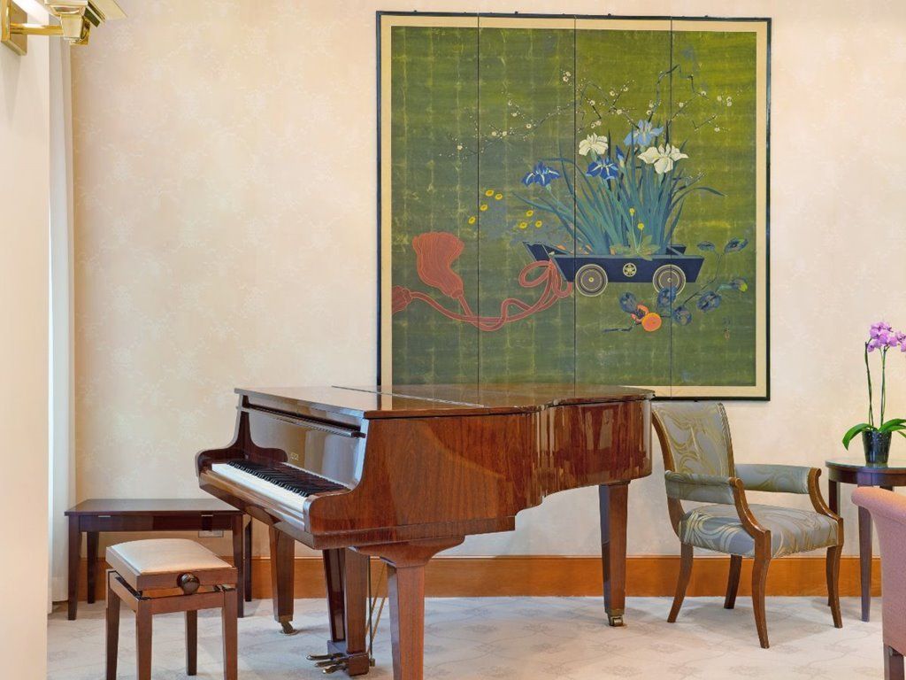 A grand piano set against a wall adorned with a colorful painting, alongside an elegant chair.