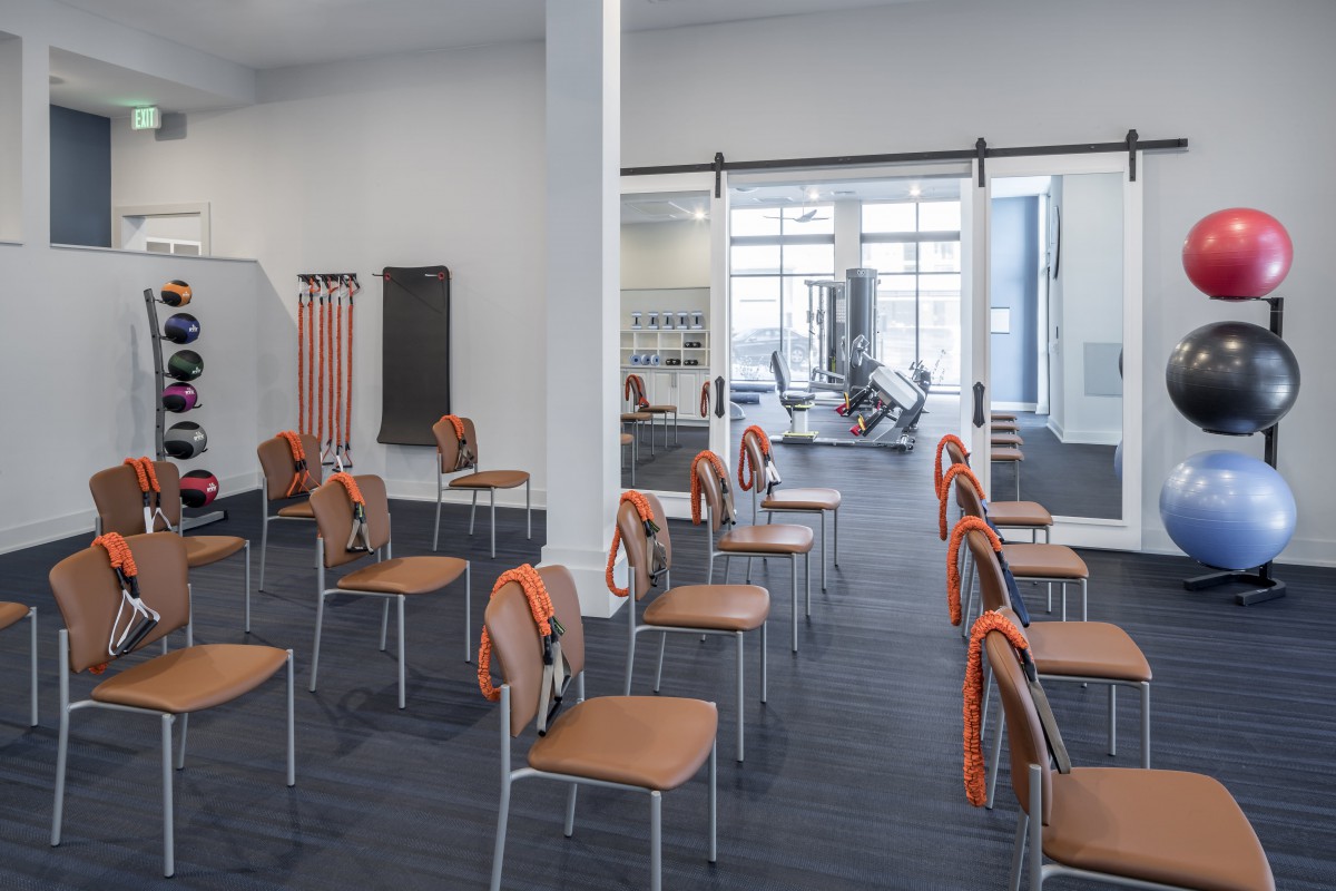 An organized training room with arranged chairs and a gym area in the background.