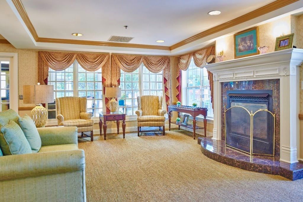 A traditional living room with a fireplace, comfortable seating, and large windows with curtains.