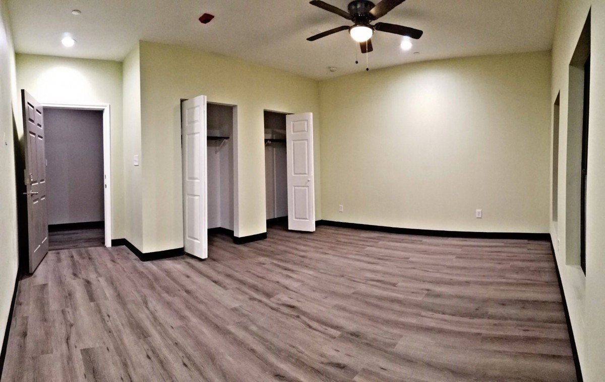 A spacious empty room with wood flooring, two open closets, and a ceiling fan.