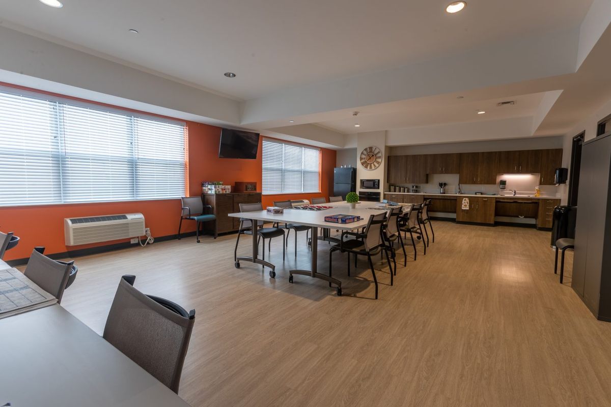 A modern open-plan kitchen and dining area with tables, chairs, and large windows.