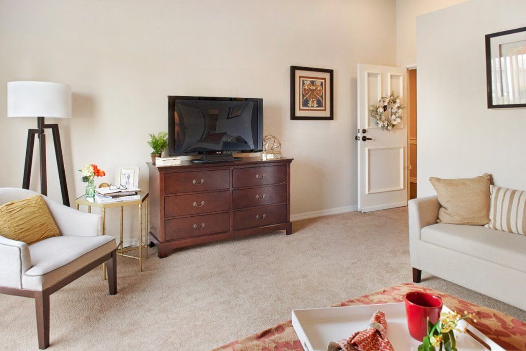 A cozy living room with a television on a wooden dresser, surrounded by comfortable furniture and decor.