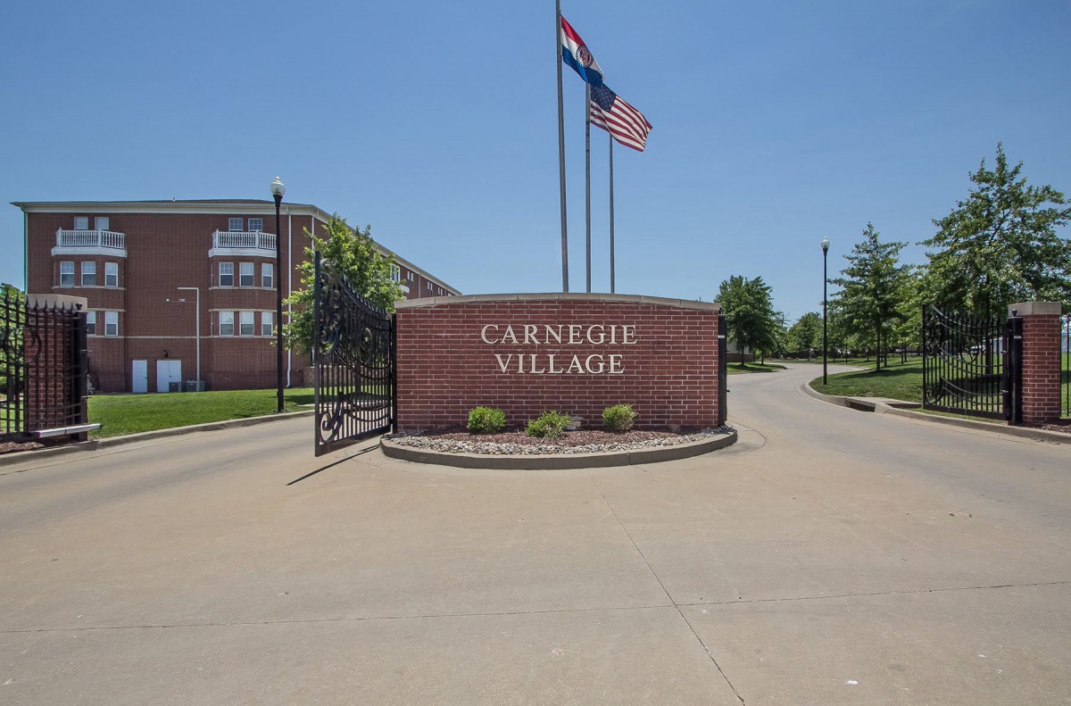 Entrance sign for Carnegie Village with flags displayed above.