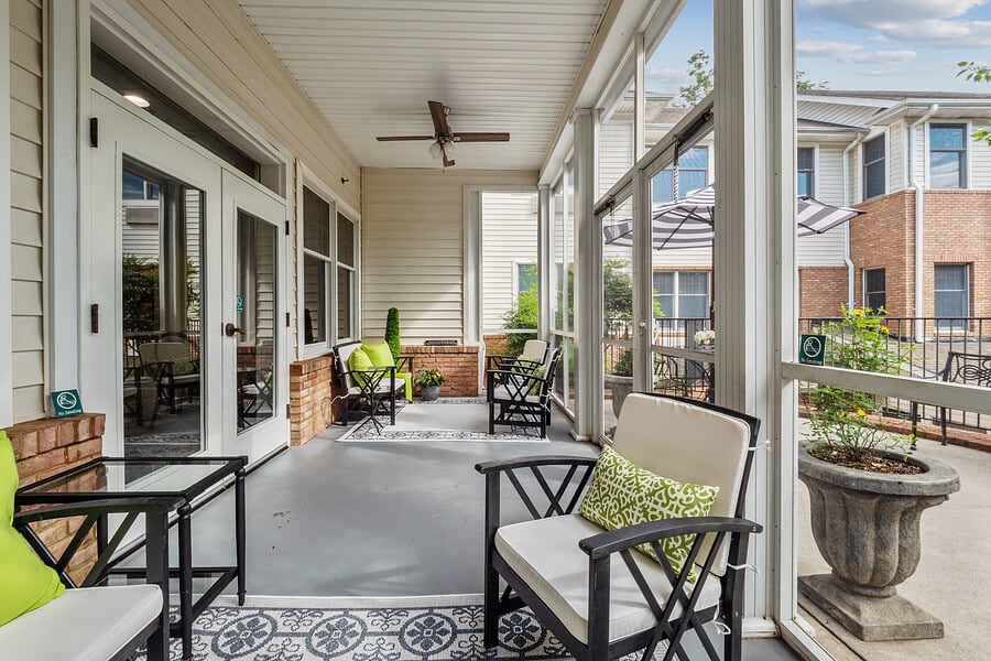 A cozy porch with comfortable seating and a ceiling fan, overlooking the outdoors.
