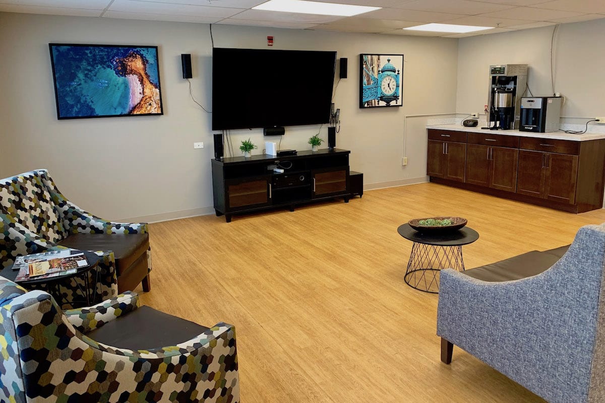 A modern living room with a large television, contemporary artwork, and comfortable seating on wooden flooring.