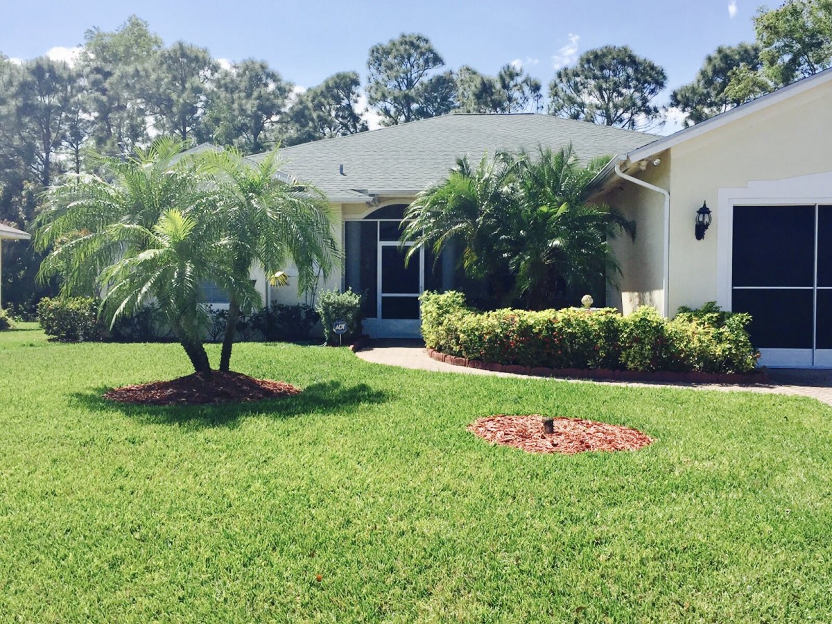 A suburban house with a well-manicured lawn and palm trees in the front yard on a sunny day.