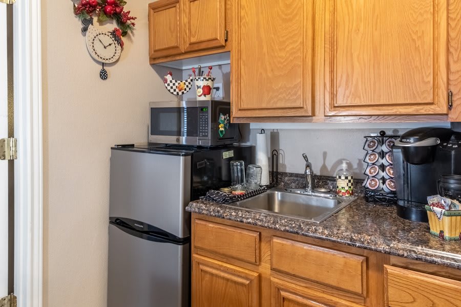 A compact kitchen area with a small fridge, microwave, wooden cabinets, and a sink.
