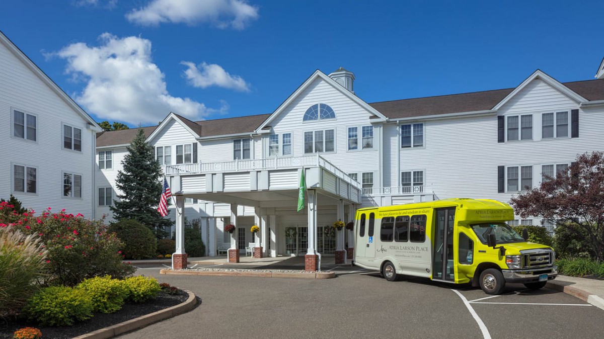 A white building with a front entrance and a yellow bus parked nearby.