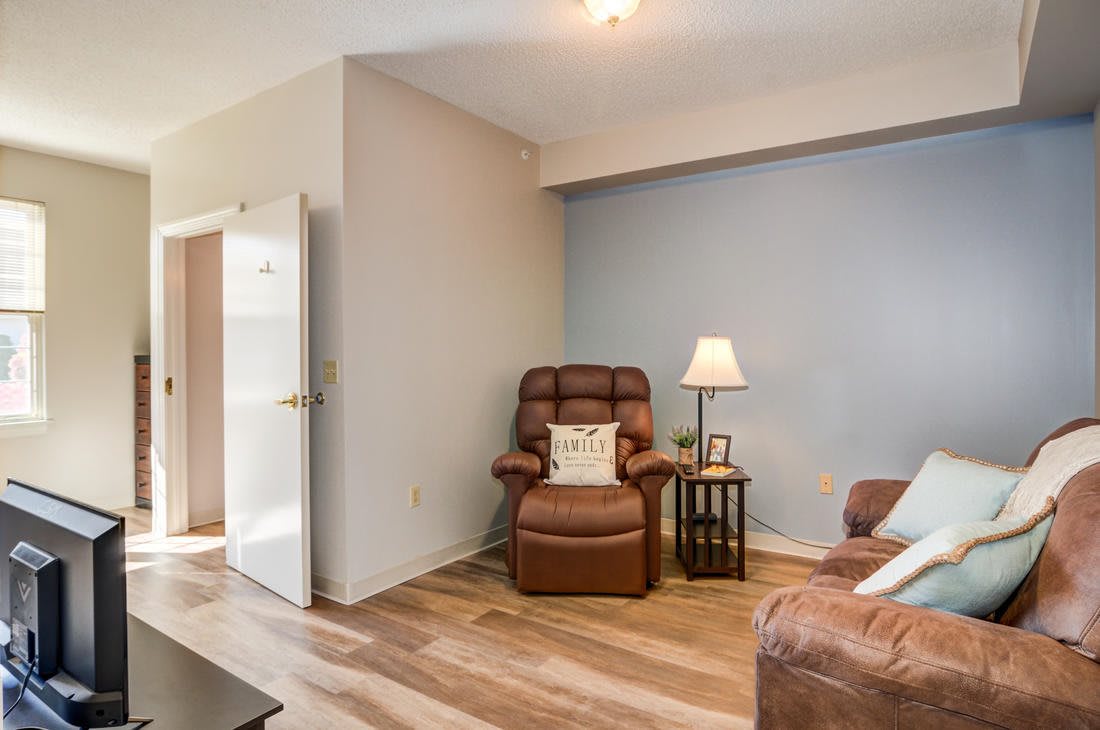 A cozy living room with a brown armchair, adjacent lamp, and wood flooring.