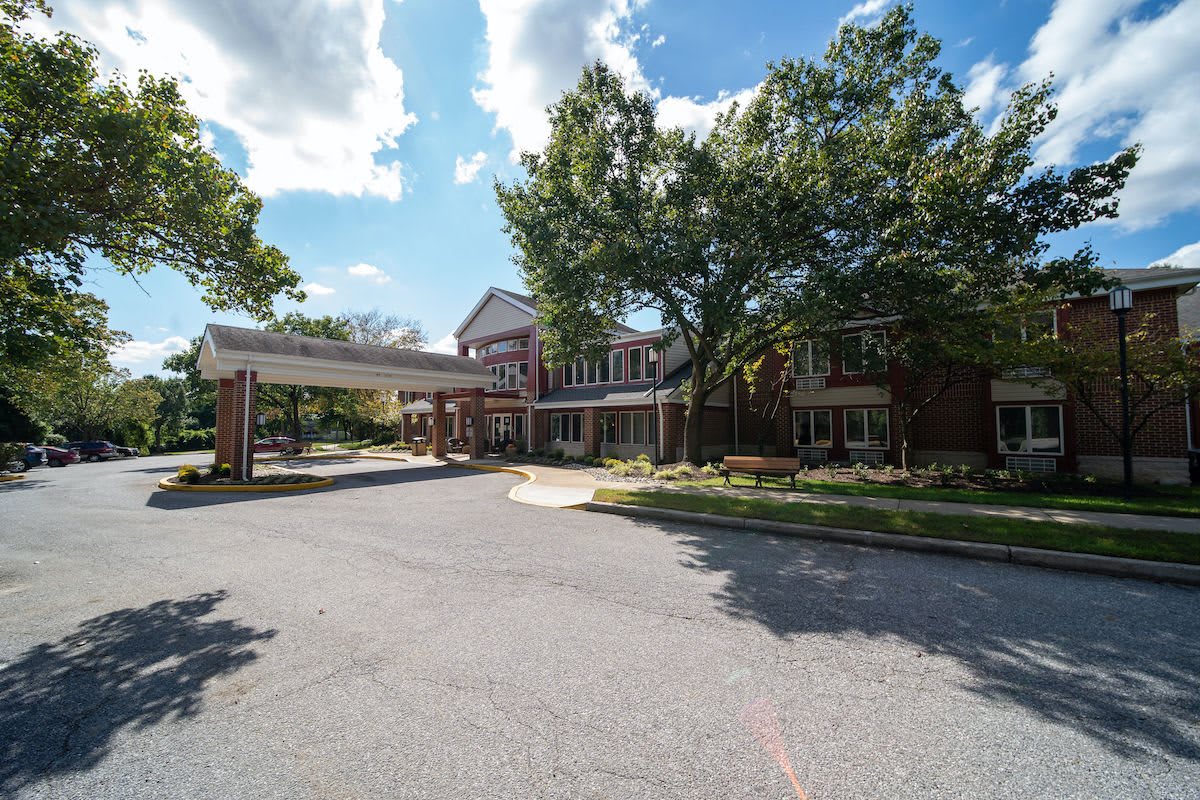 A large building with a covered entrance and surrounding trees on a sunny day.