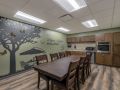 A kitchen with a large wooden dining table and chairs, featuring a wall mural and wood flooring.
