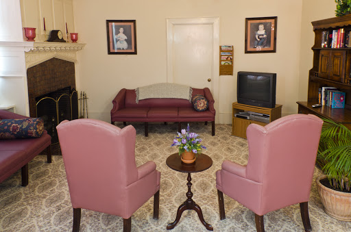 A cozy living room setup featuring a sofa, two pink armchairs, and a small coffee table with flowers.