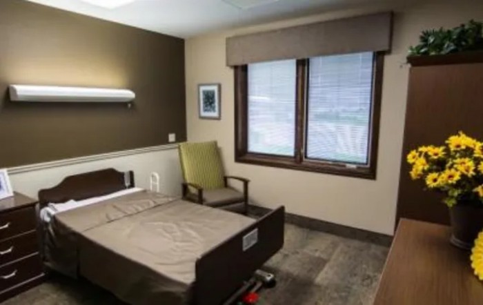 A hospital room with a bed, chair, and window.