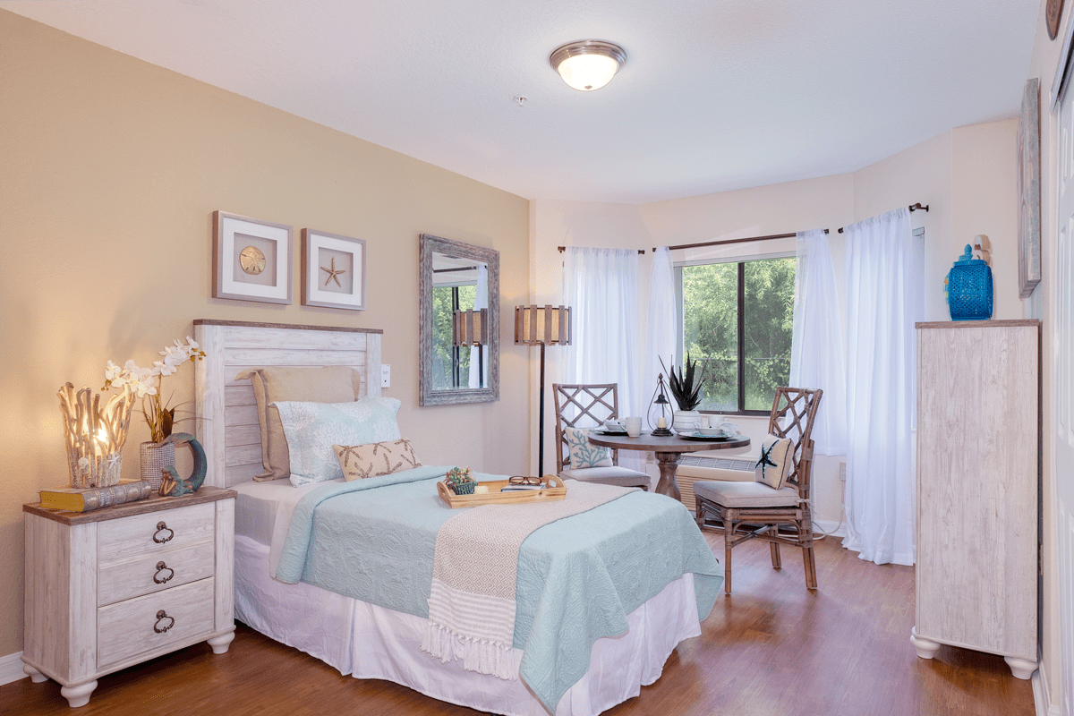 A cozy bedroom with a neatly made bed, stylish decor, and ample natural light from a large window.
