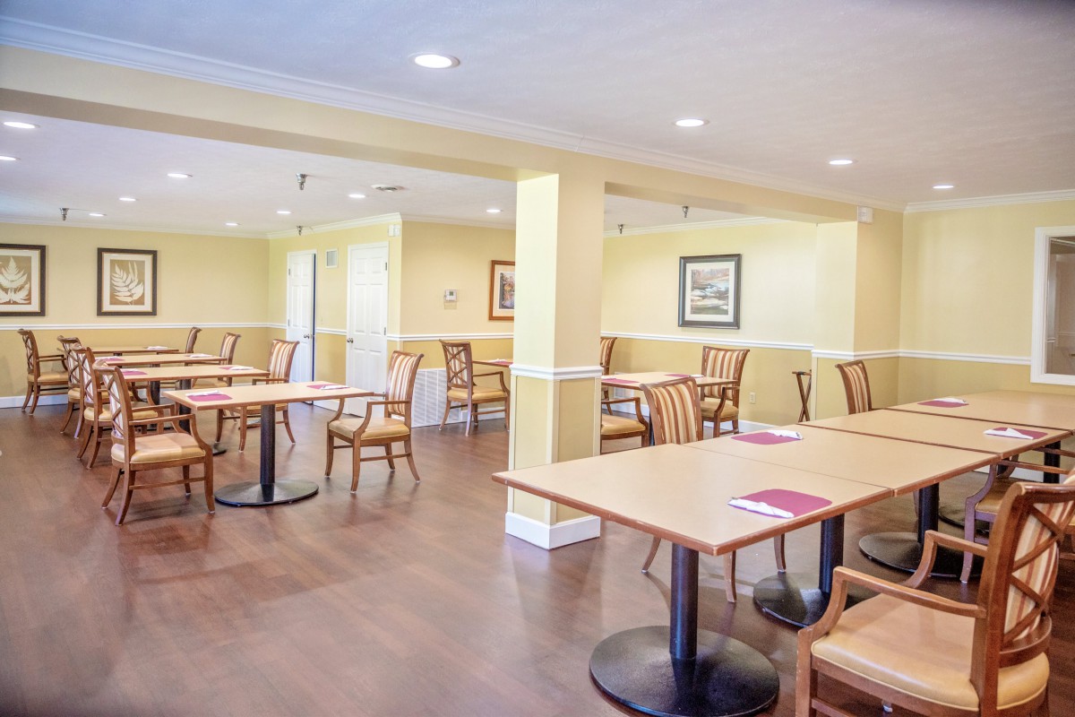 A neatly arranged dining area with wooden tables and chairs, illuminated by bright lighting.