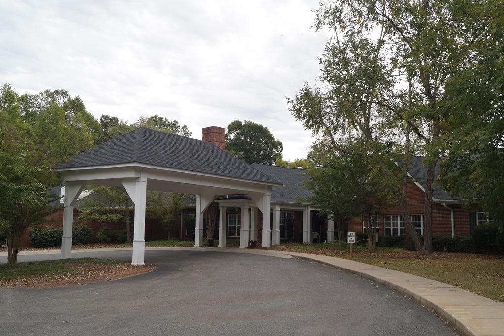 A building with a covered entrance and a driveway, surrounded by trees.