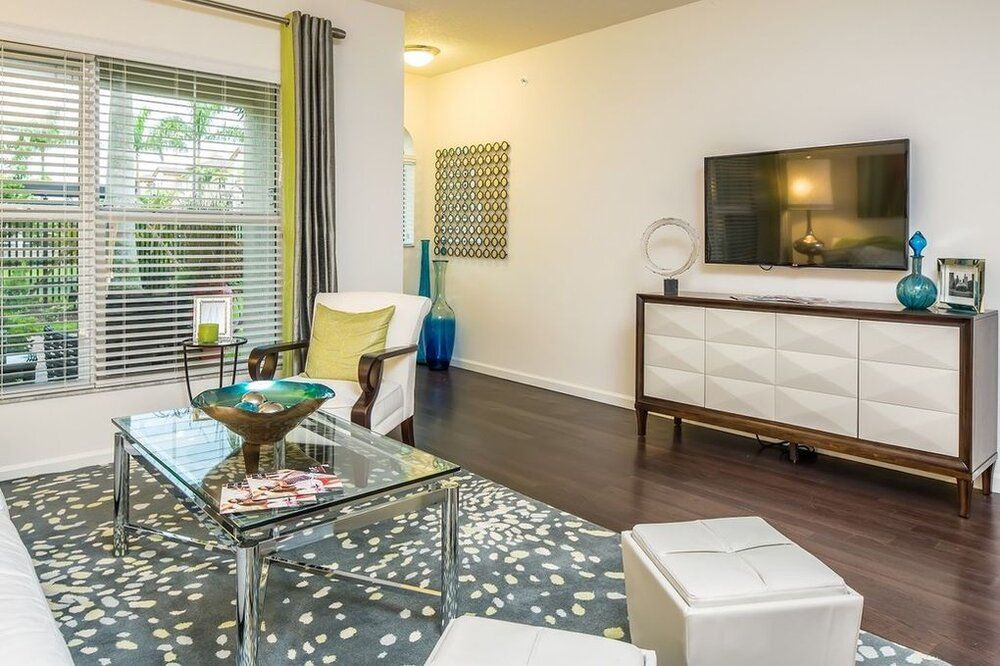 A modern living room with stylish furniture, a TV mounted on the wall, and a glass coffee table.