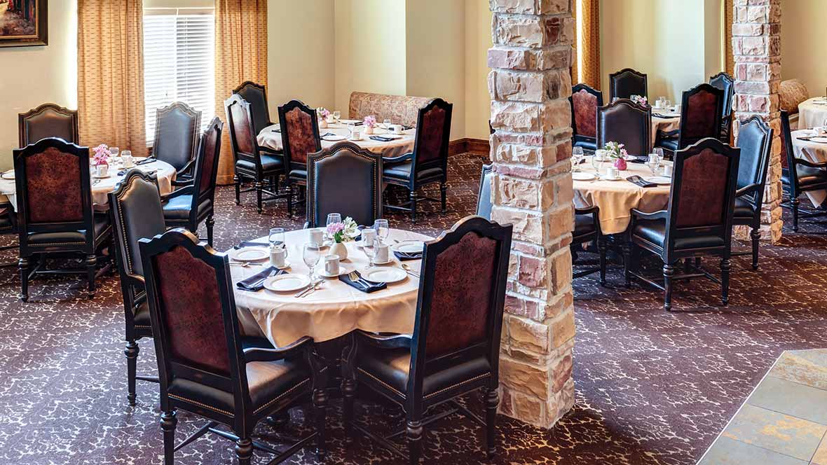 An elegantly set dining area with multiple round tables and classic chairs.