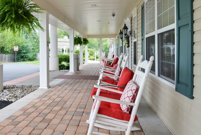 A charming porch with white rocking chairs adorned with red cushions, creating a welcoming outdoor space.